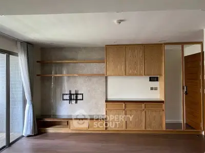 Spacious living room with built-in wooden shelves and TV mount, featuring large window for natural light.
