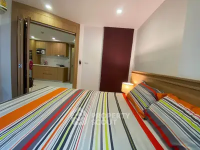 Modern bedroom with colorful striped bedding and view into a sleek kitchen area.
