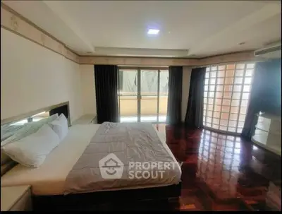 Spacious bedroom with elegant wooden flooring and large windows for natural light.