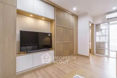 Modern living room with sleek wooden paneling and large TV, showcasing minimalist design and natural light.