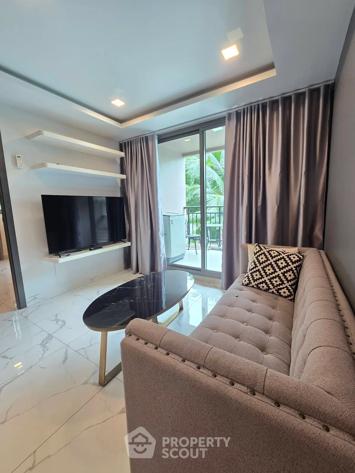 Modern living room with sleek furniture and large windows opening to a balcony with lush greenery view.