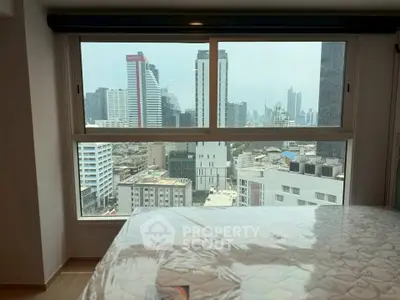 Spacious bedroom with stunning city view from large window in modern high-rise apartment.