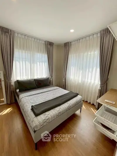 Bright and cozy bedroom with large windows and elegant curtains, perfect for relaxation.