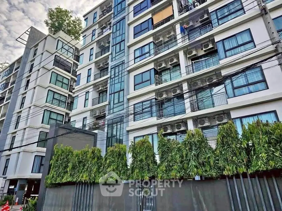 Modern multi-story apartment building with lush greenery and sleek design.