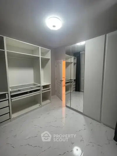 Spacious walk-in closet with modern white cabinetry and sleek mirrored doors.