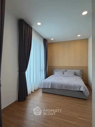 Modern bedroom with elegant curtains and wooden flooring, featuring a cozy bed and soft lighting.