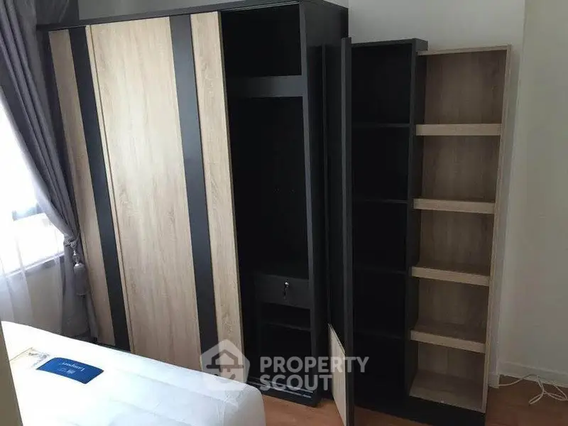 Modern bedroom with sleek wardrobe and bookshelf, featuring natural light and contemporary design.