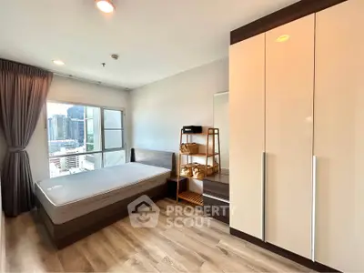 Modern bedroom with city view, featuring sleek wardrobe and wooden flooring in urban apartment.
