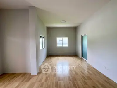 Spacious empty room with wooden flooring and large windows, perfect for customization.