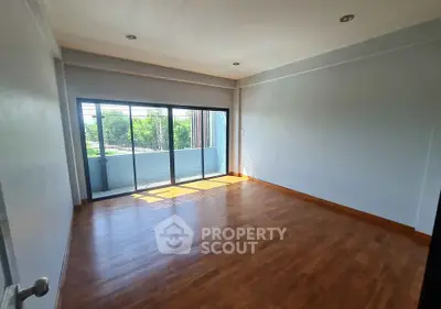 Spacious empty room with wooden flooring and large windows offering natural light and outdoor view.