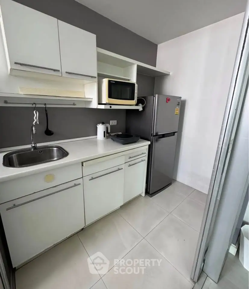 Modern compact kitchen with sleek white cabinets and stainless steel appliances in a stylish apartment.