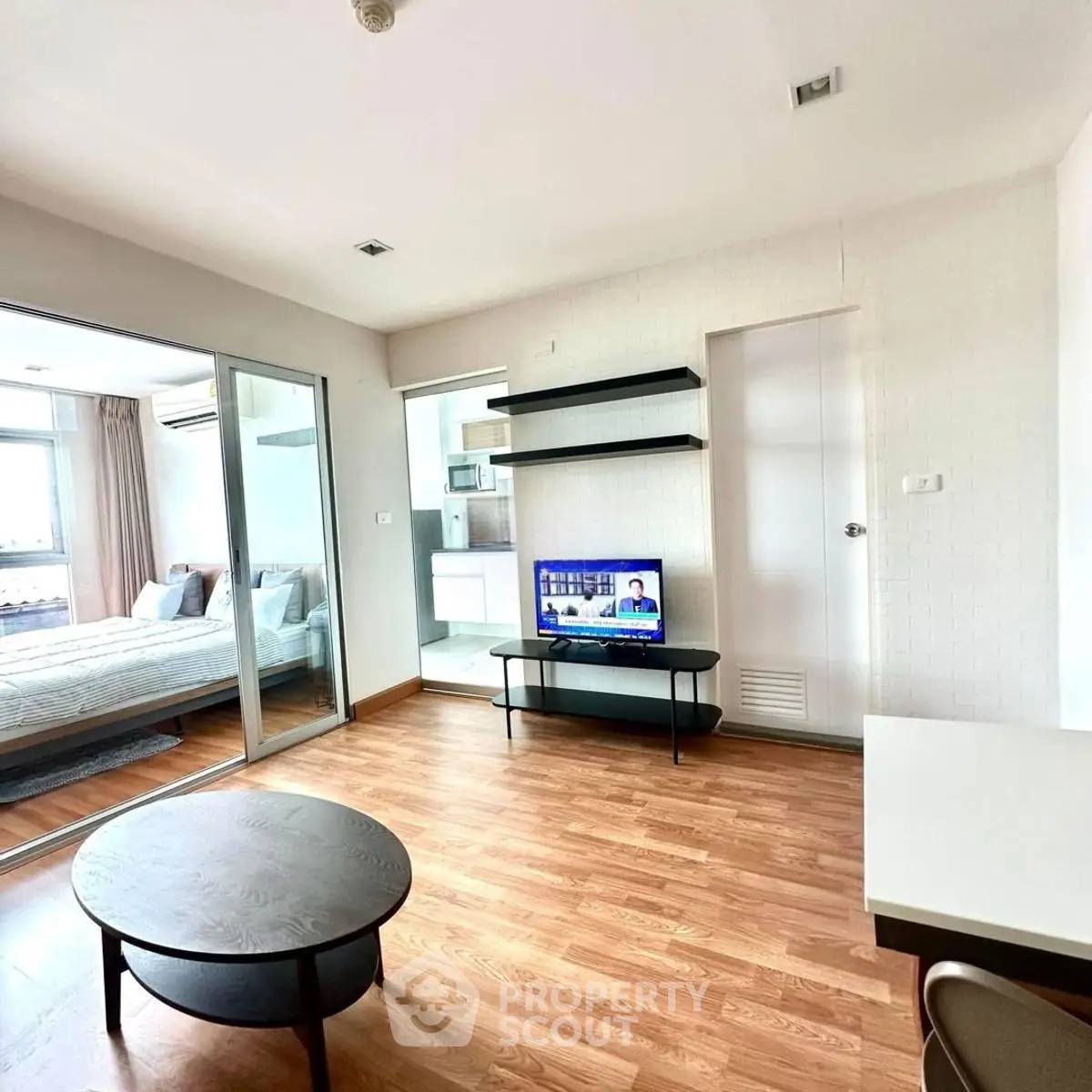 Modern living room with wooden flooring and view into a cozy bedroom through glass doors.