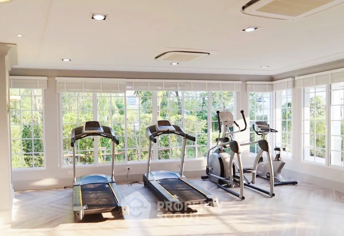 Spacious home gym with modern equipment and large windows offering garden views.