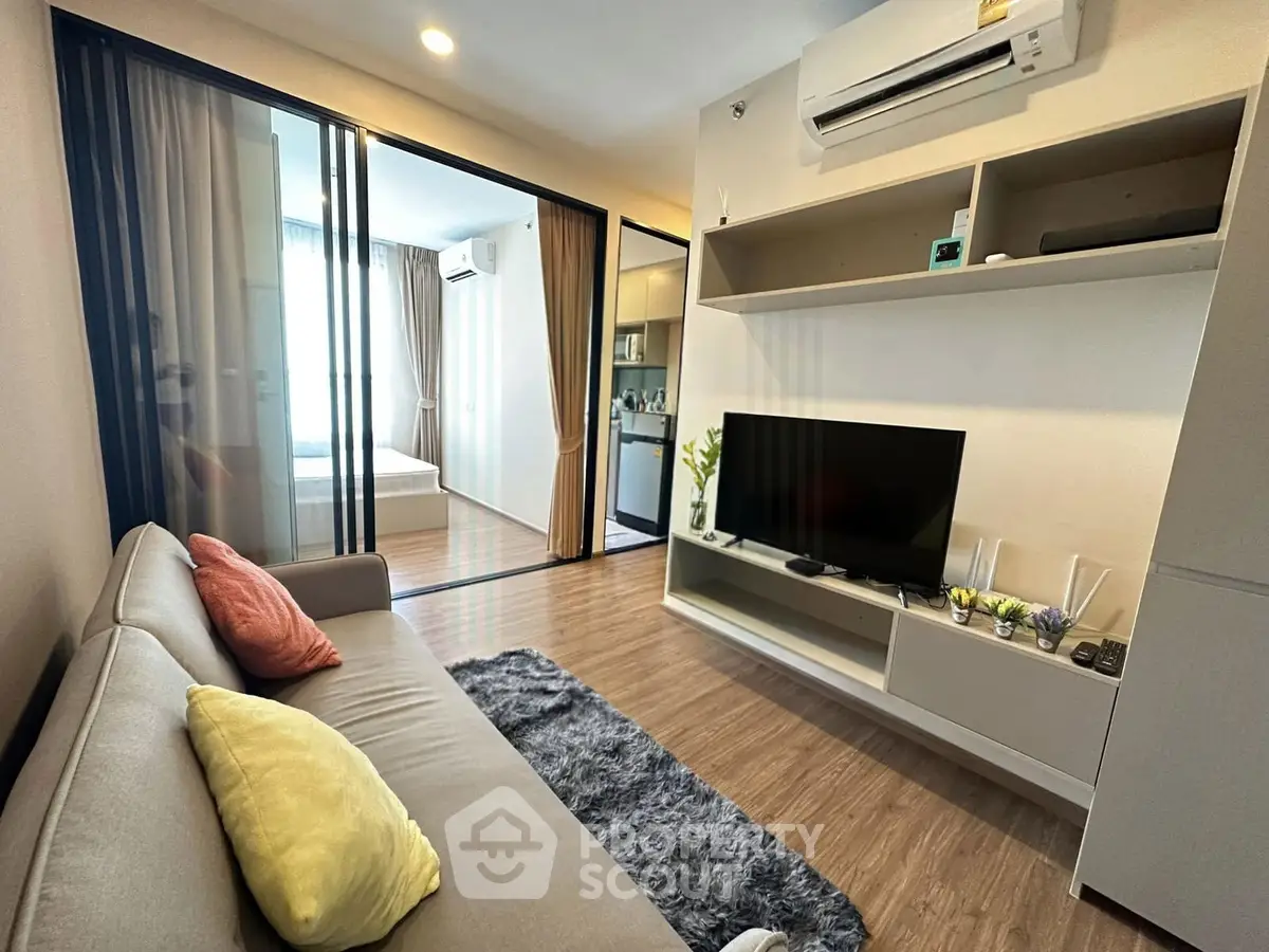 Modern living room with cozy sofa, TV, and open view to bedroom in stylish apartment.