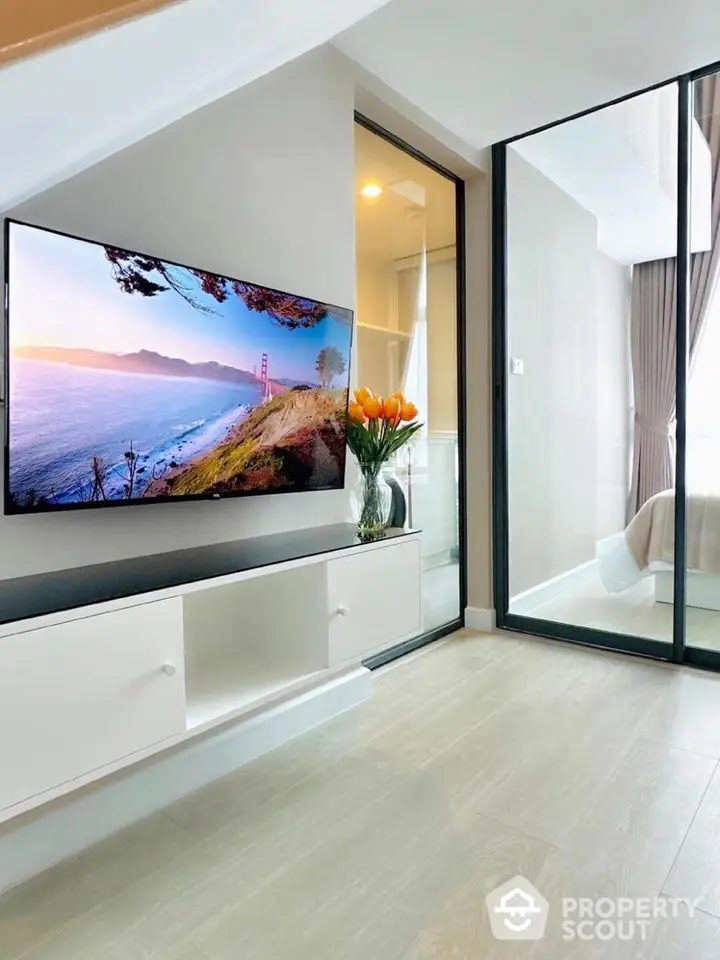 Modern living room with wall-mounted TV and glass door leading to bedroom