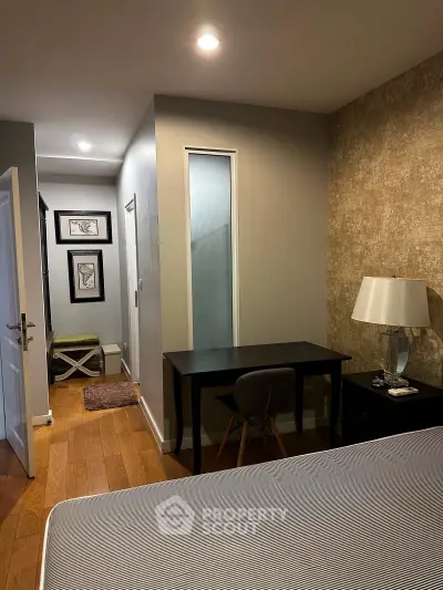 Cozy bedroom with modern decor and study area, featuring elegant lighting and hardwood floors.