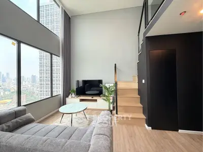 Modern loft apartment with large windows and city view, featuring a cozy living area and stylish staircase.