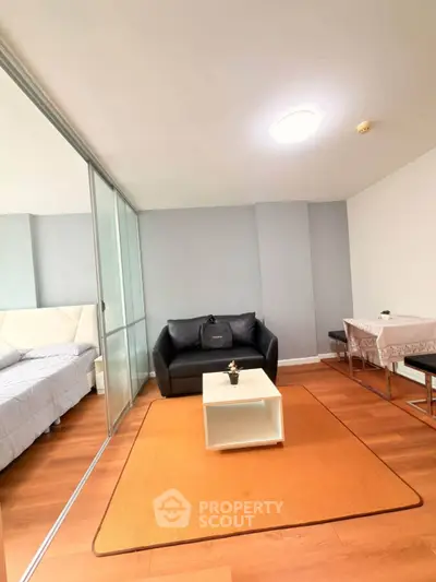 Modern living room with cozy seating and dining area, featuring sleek glass partition and warm wooden flooring.