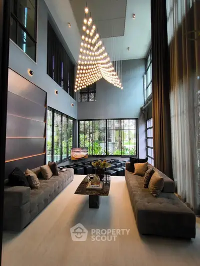 Luxurious modern living room with high ceilings, elegant chandelier, and plush sofas overlooking a garden view.