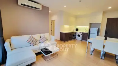 Modern living room with open kitchen, featuring cozy sofa and dining area.