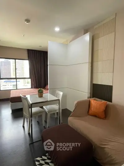 Modern studio apartment with cozy living area and city view, featuring a dining table and comfortable seating.