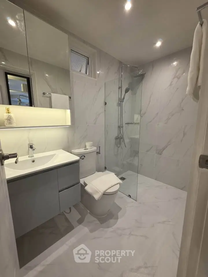 Modern bathroom with glass shower and sleek fixtures in elegant marble design.