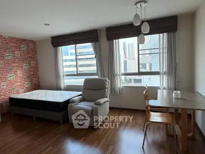 Modern studio apartment with large windows, wooden flooring, and stylish furniture in a city setting.