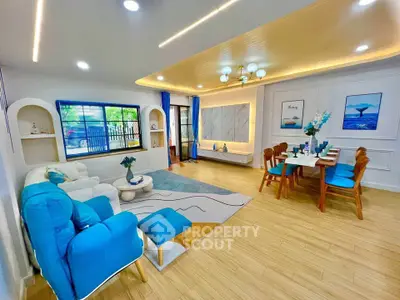 Spacious modern living room with vibrant decor and dining area, featuring stylish lighting and large windows.
