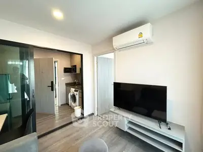 Modern living room with sleek TV and air conditioning, adjacent to a compact kitchen with washing machine.