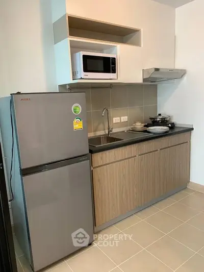 Modern kitchen with sleek cabinets, stainless steel fridge, microwave, and electric stove in a compact layout.