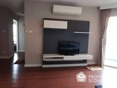 Spacious living room with polished hardwood floors and modern entertainment wall unit, bathed in natural light from large windows.