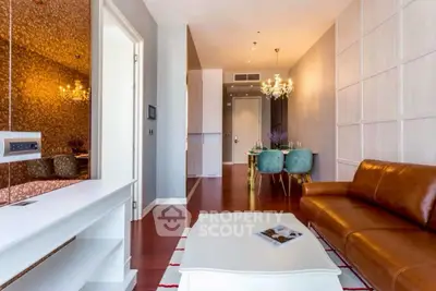 Modern living room with leather sofa, elegant chandelier, and open dining area in stylish apartment.
