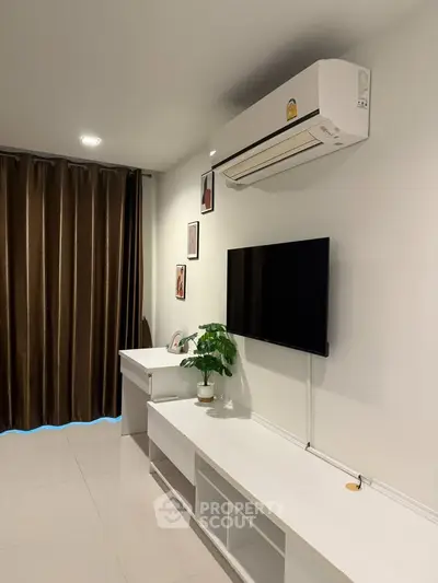 Modern living room with sleek white furniture and wall-mounted TV, featuring elegant decor and air conditioning.