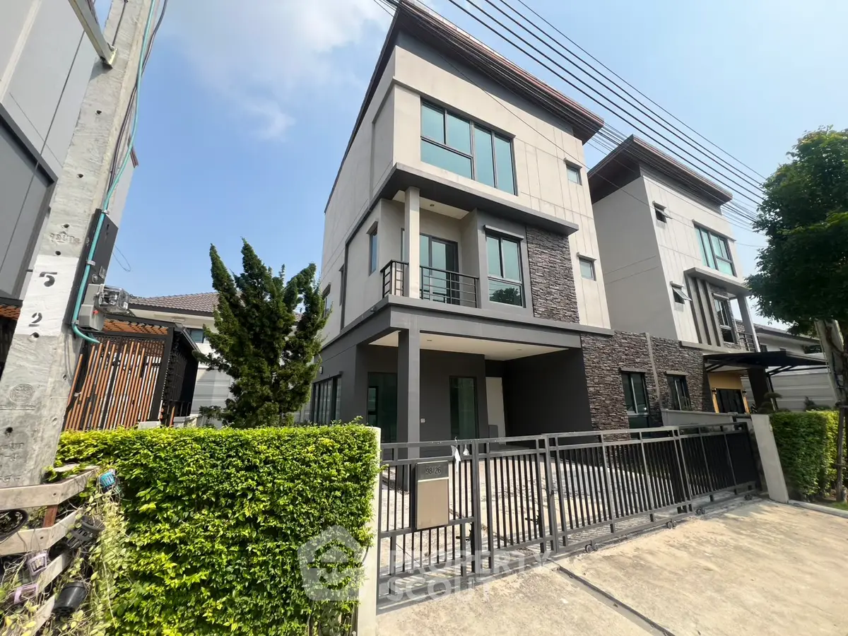 Modern three-story house with sleek design and gated entrance in a suburban neighborhood.