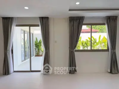 Spacious living room with large windows and sliding doors opening to a lush garden view.