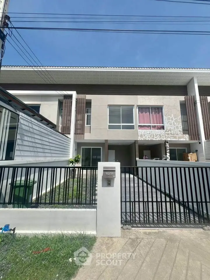 Modern townhouse exterior with gated entrance and driveway under clear blue sky.