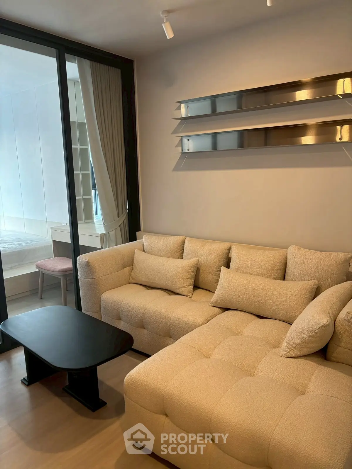 Modern living room with plush beige sofa and sleek black coffee table, adjacent to a stylish bedroom.