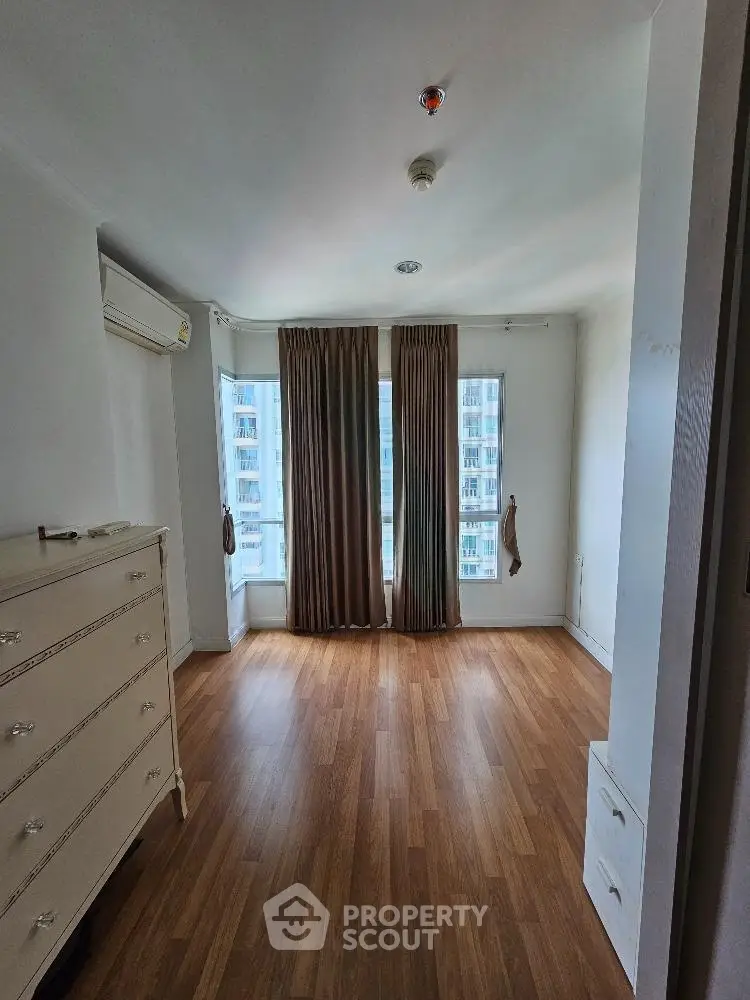 Spacious bedroom with wooden flooring and large windows offering city views.