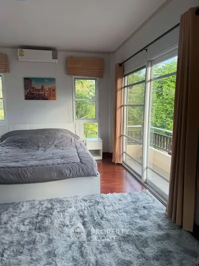 Spacious bedroom with large windows and balcony access, featuring lush green views.