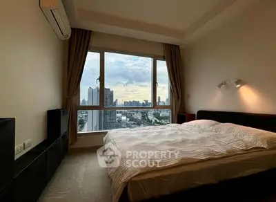 Spacious bedroom with stunning city view from large window, modern furnishings, and cozy ambiance.