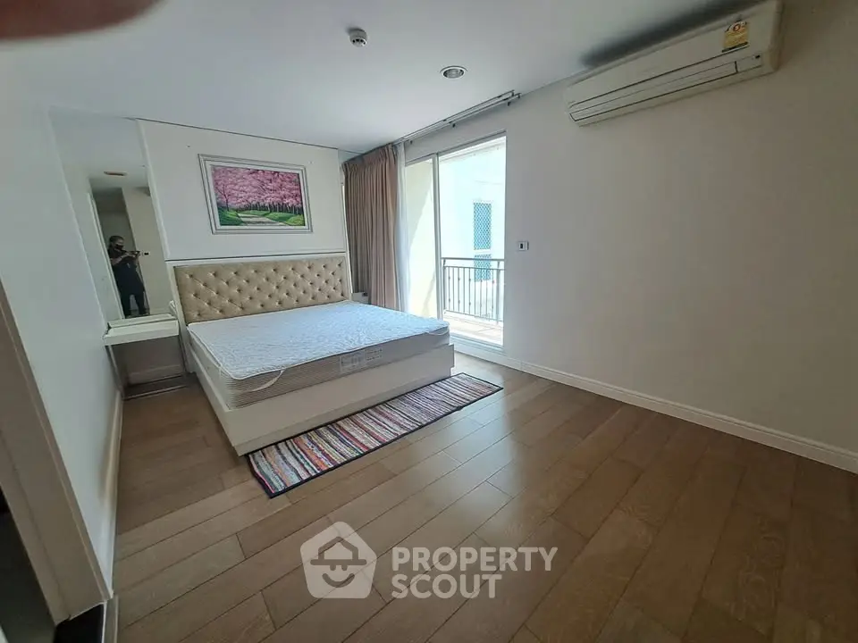 Spacious bedroom with wooden flooring and balcony access in modern apartment