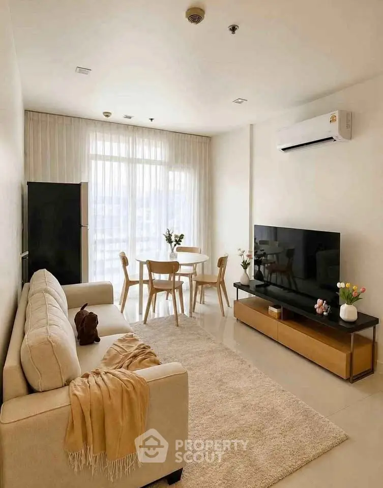 Modern living room with cozy beige sofa, large TV, and dining area with natural light.