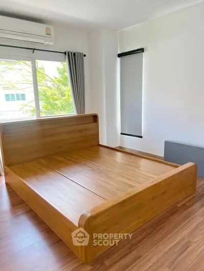 Spacious bedroom with wooden flooring and large window for natural light.