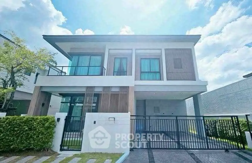 Modern two-story house with sleek design and gated entrance, featuring large windows and a spacious driveway.