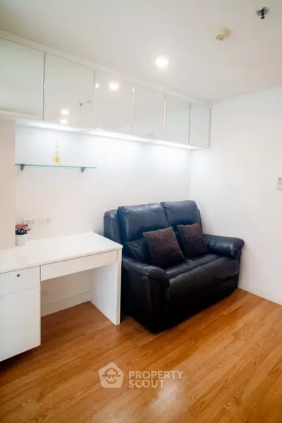 Cozy living room with sleek black sofa and modern white desk, perfect for a compact urban apartment.