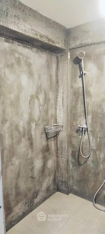 Modern industrial-style bathroom with concrete walls and sleek shower fixtures.