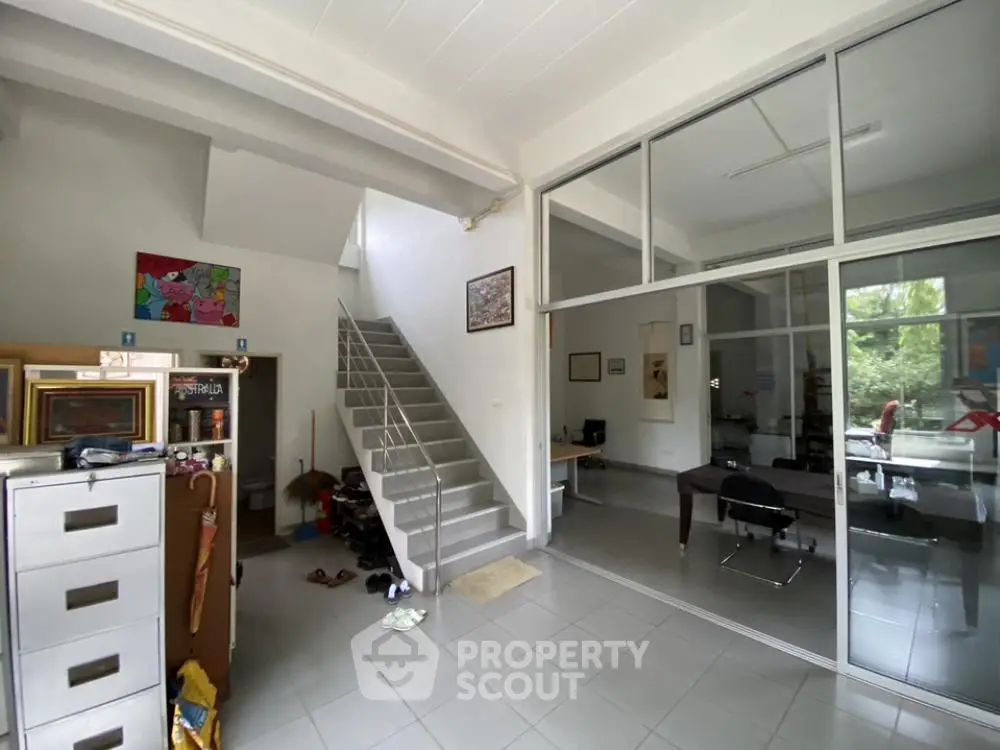 Spacious and bright living area with high ceilings, sleek staircase, and large glass partitions creating a modern open-plan space ideal for entertaining and family life.
