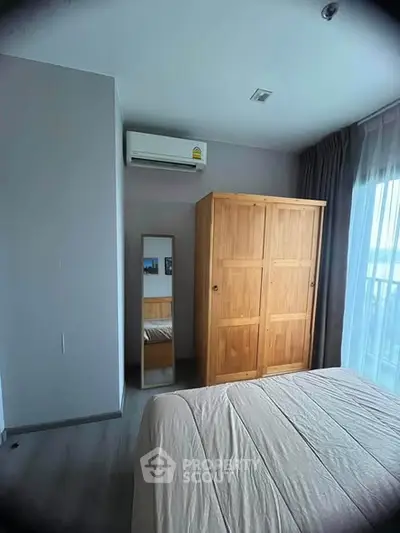 Cozy bedroom with wooden wardrobe and air conditioning, featuring natural light from large window.
