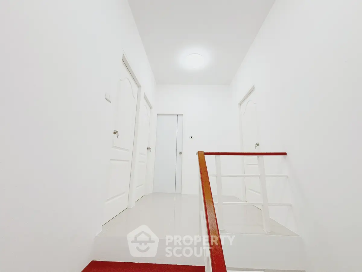 Bright white corridor with three doors and a staircase, showcasing minimalist design.
