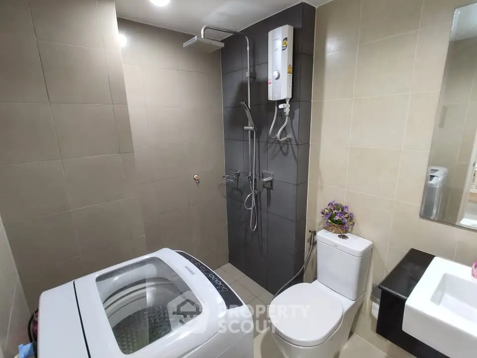 Modern bathroom with washing machine and shower in a sleek, tiled design.
